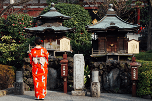 Kimono Tradition - Frau im rot-orangen Kimono vor einem Schrein.