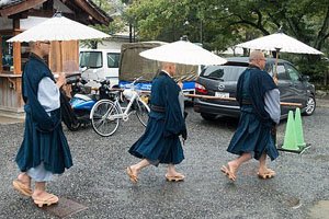 Drei Mönsche mit Regenschirmen die nach rechts laufen.